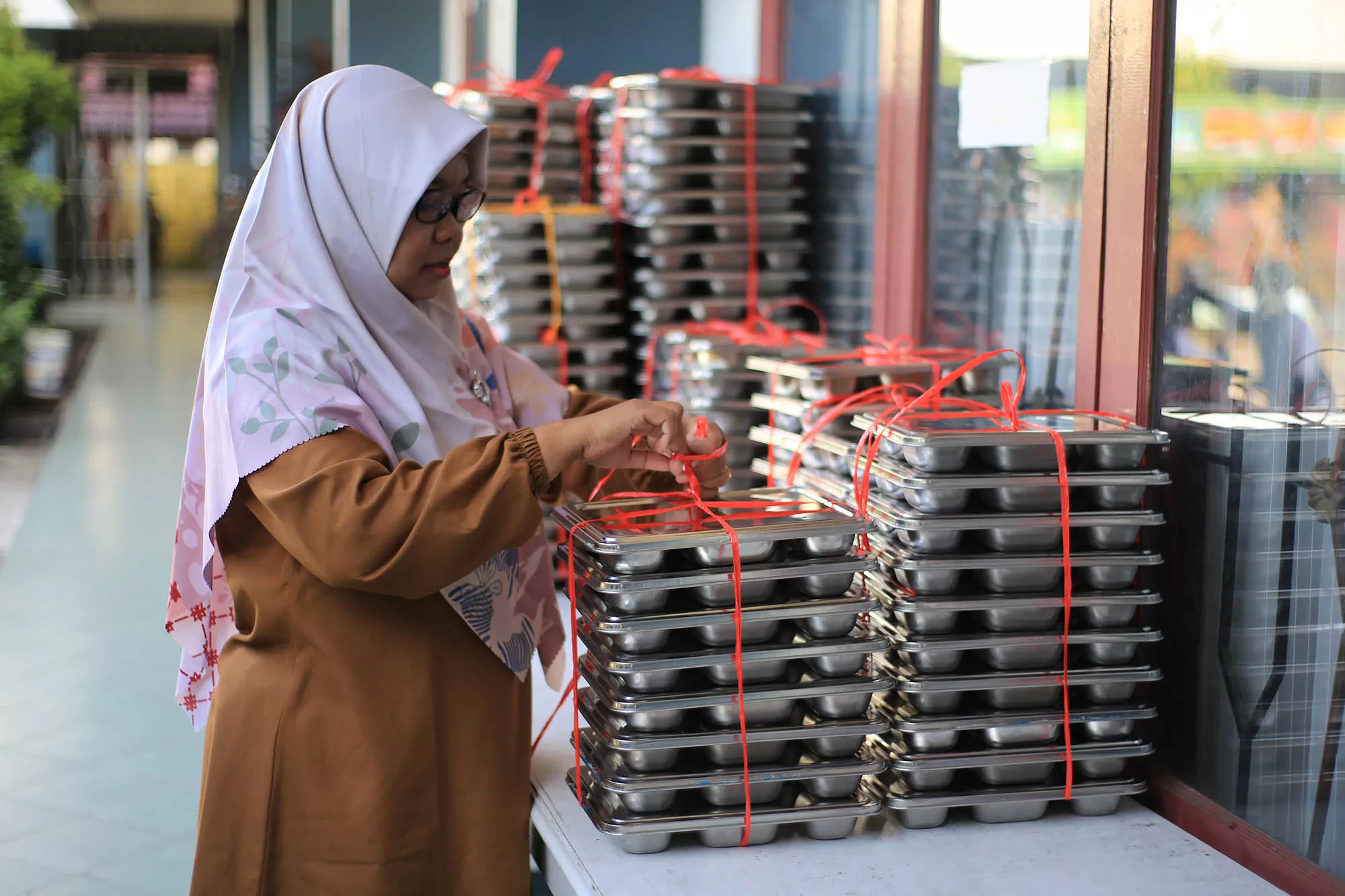 Seorang guru membawa  ompreng  berisi menu makanan bergizi gratis (MBG)  di SDN 20 Banda Aceh, Selasa (19/5/2026). Badan Gizi Nasional mengingatkan  SPPG yang belum mampu memenuhi target penerima kategori ibu hamil, ibu menyusui, dan balita (3B) di wilayahnya akan dikenakan penghentian operasional sementara atau suspend. Aentenews Foto/Ampelsa.