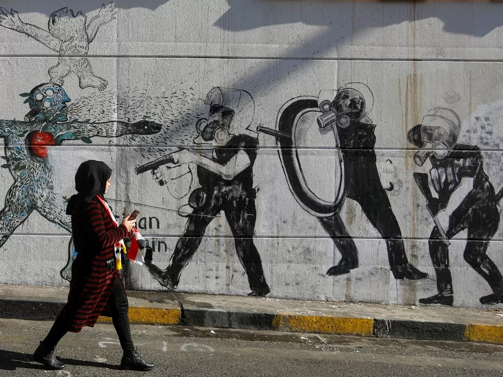 Demonstran wanita berjalan melewati mural saat berlangsungnya protes anti pemerintah di Baghdad, Irak. REUTERS/Khalid al-Mousily