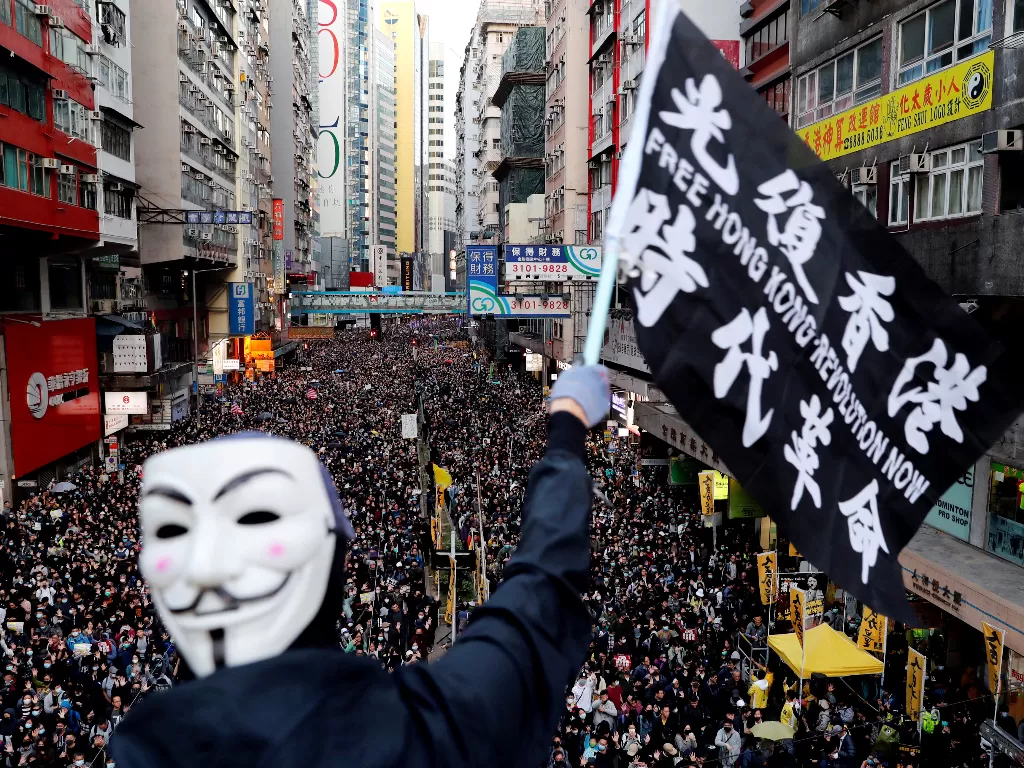 Seorang pengunjuk rasa memakai topen Guy Fawkes mengibarkan bendera saat demonstrasi Hari Hak Asasi Manusia, yang diselenggarakan oleh Civil Human Right Front, di Hong Kong, 8 Desember 2019. REUTERS/Danish Siddiqui