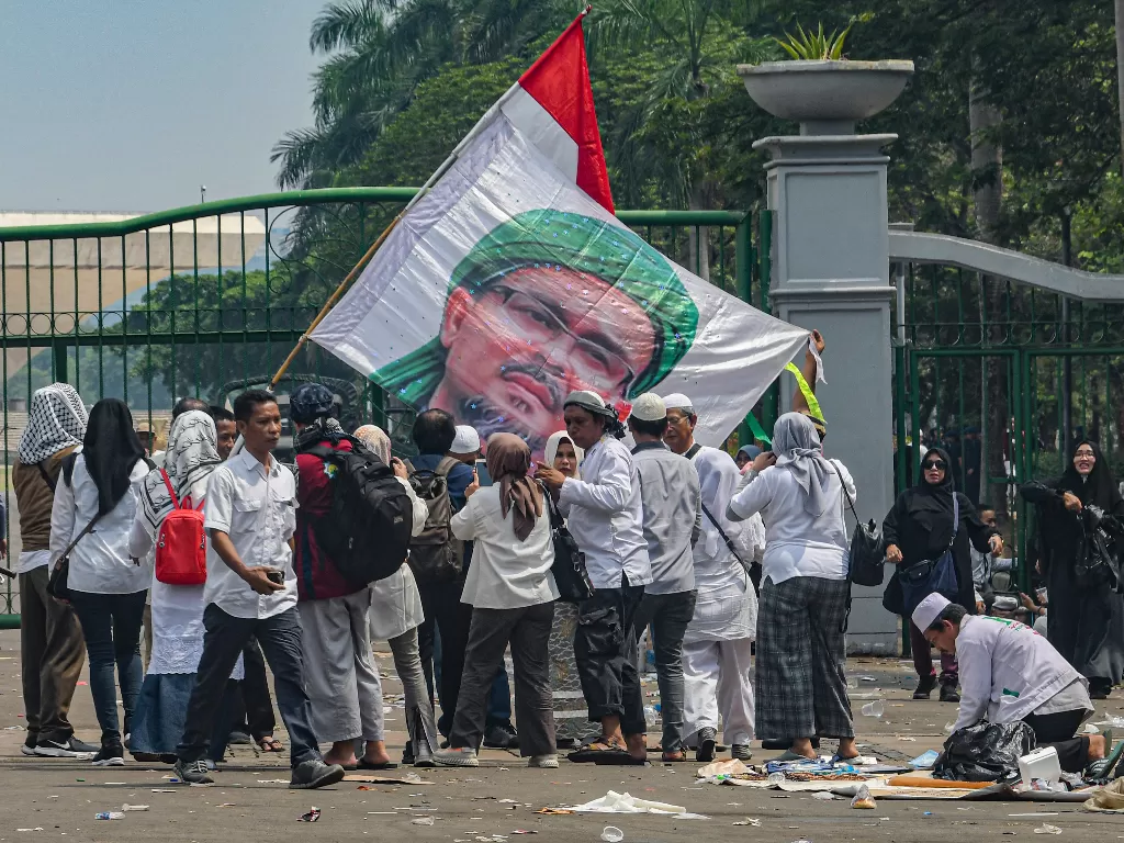 Peserta aksi reuni 212 berfoto dengan latar belakang foto Imam FPI Habib Rizieq usai mengikuti aksi tersebut di kawasan Monas, Jakarta, Senin (2/12/2019). (Antara/Muhammad Adimaja)