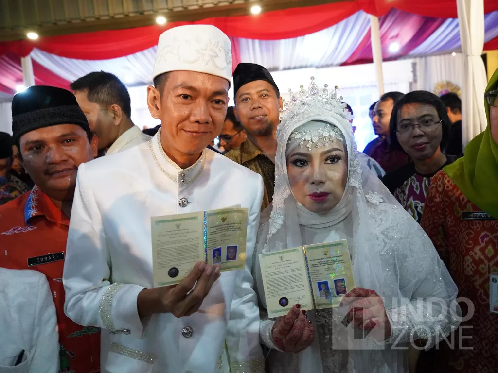 Sepasang pengantin menunjukkan buku nikah saat mengikuti Nikah Massal di halaman Gedung Balai Kota DKI Jakarta, Selasa (31/12). INDOZONE/Arya Manggala