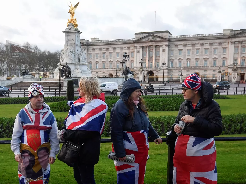 Penggemar kerajaan mengenakan bendera Inggris terlihat di luar Istana Buckingham, London, Inggris, Kamis (9/1/2020). (REUTERS/Toby Melville)