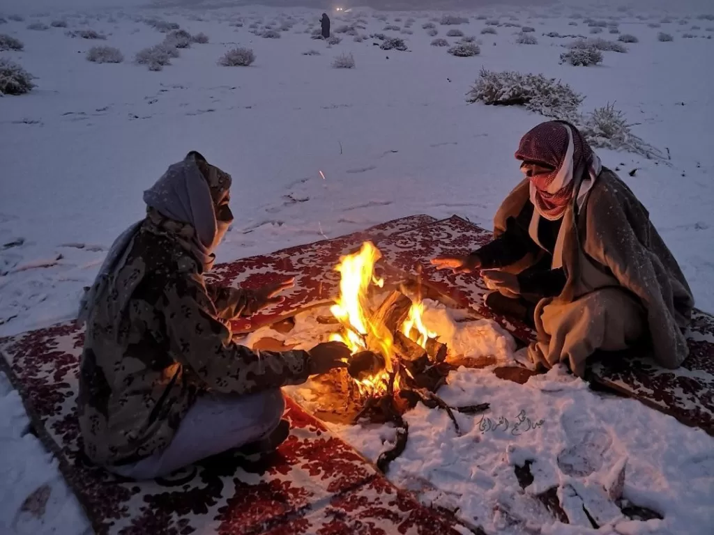 Dua pria di Tabuk, Arab Saudi, duduk menghangatkan diri di dekat api dengan salju di sekitar mereka. (photo/Twitter/@fo0fo081)