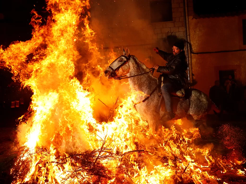 Peserta menunggang kuda melewati kobaran api dalam Festival Luminarias di Desa San Bartolome de Pinares, Spanyol, Kamis (16/1/2020). (REUTERS/Juan Medina)