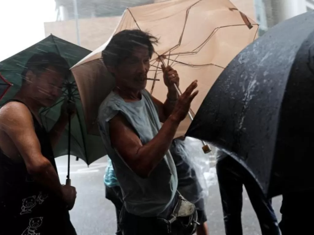 Beberapa orang terlihat kesulitan menggunakan payung di tengah hujan disertai angin kencang (REUTERS/Tyrone Siu).