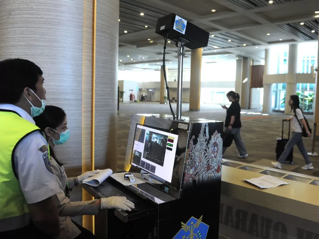 Petugas memantau suhu tubuh penumpang menggunakan alat pemindai suhu tubuh di Terminal Kedatangan Internasional Bandara Internasional I Gusti Ngurah Rai. (ANTARA FOTO/Fikri Yusuf)