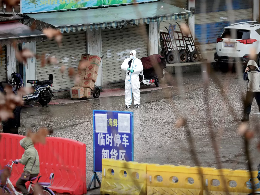 Seorang pekerja dengan kostum pengamanan berada di depan sebuah pasar seafood di Wuhan, China. (REUTERS/Darley Shen)