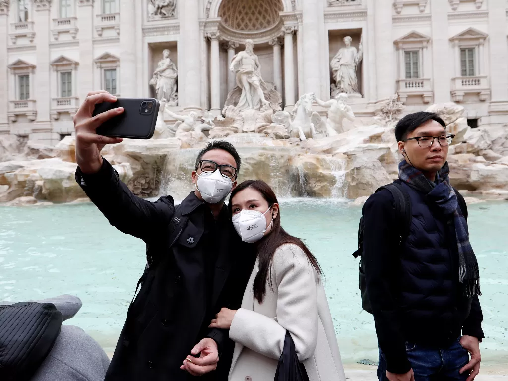 Sepasang turis berwajah Asia yang mengenakan masker berswafoto di depan Air Mancur Trevi, Roma, Italia, Jumat (31/1). (REUTERS/Remo Casilli) 