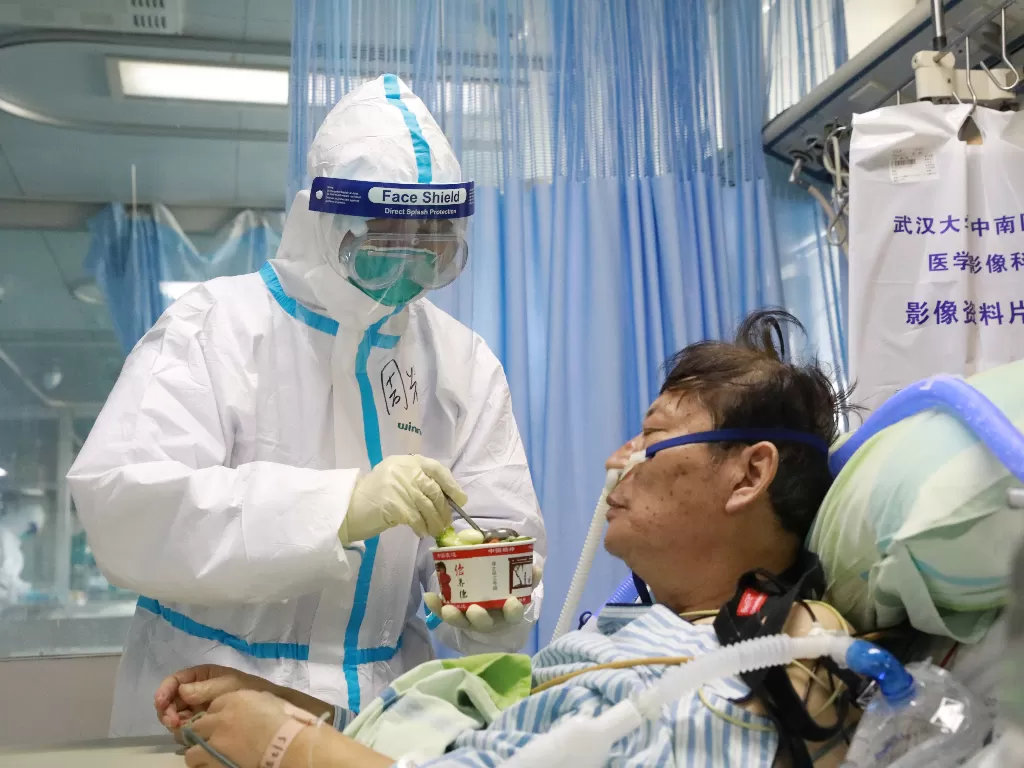 Perawat dalam setelan pelindung memberi makan pasien coronavirus baru di dalam bangsal terisolasi di Rumah Sakit Zhongnan, Universitas Wuhan. (photo/REUTERS/China Daily)
