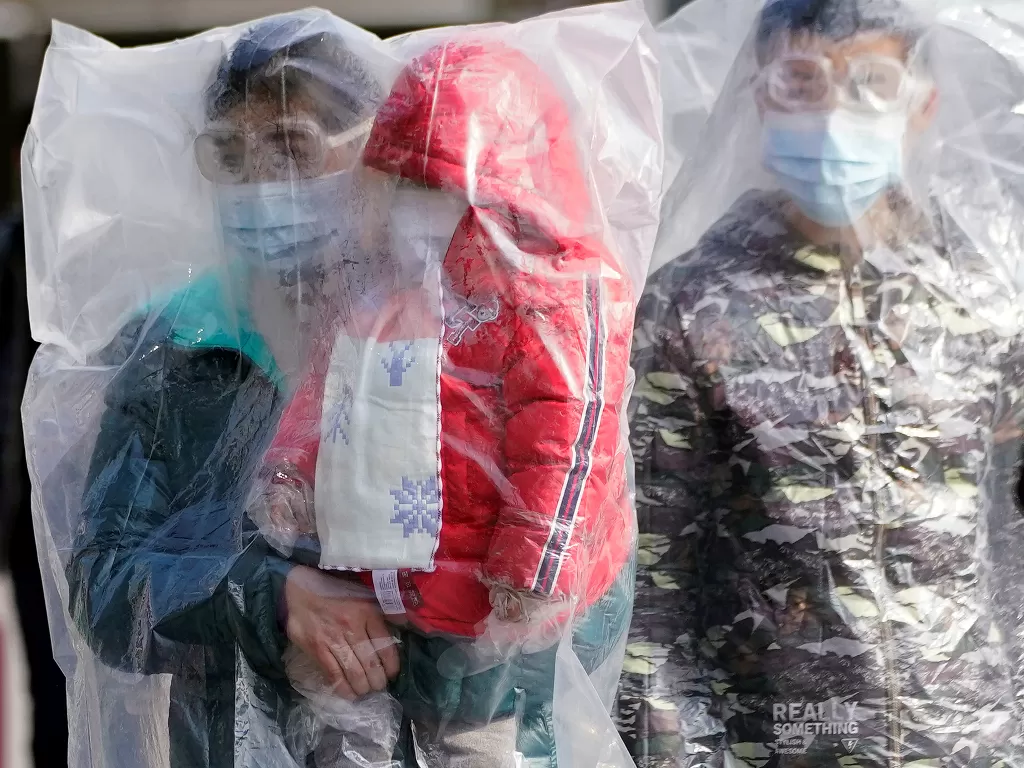 Penumpang yang mengenakan masker dan ditutupi dengan kantong plastik berjalan di luar stasiun kereta api di Shanghai, Tiongkok, saat negara tersebut dilanda wabah virus korona baru, Minggu (9/2/2020). (REUTERS/Aly Song)