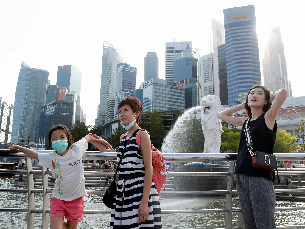 Sejumlah turis mengenakan masker berfoto di kawasan Merlion Park, Teluk Marina di Singapura, Selasa, (28/1). (REUTERS/Feline Lim)