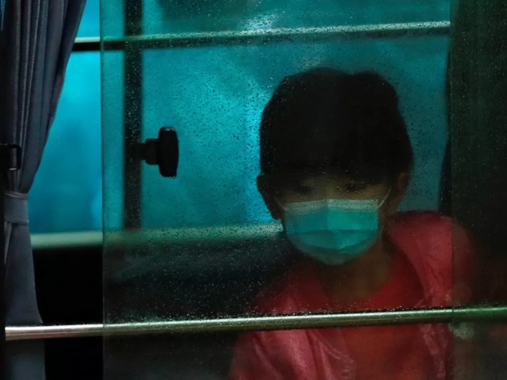 Seorang anak memakai masker saat duduk di dalam kendaraan membawa warga yang dievakuasi dari gedung perumahan umum, setelah mewabahnya virus novel korona, di depan Hong Mei House, di Cheung Hong Estate, Hong Kong, China, Selasa (11/2/2020). (Photo/REUTERS