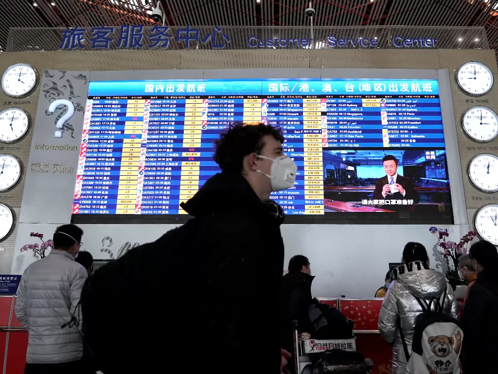 Seorang penumpang pesawat mengenakan masker berjalan di depan papan informasi jadwal keberangkatan di Bandara Internasional Beijing, Beijing, (1/2). (REUTERS/Jason Lee)