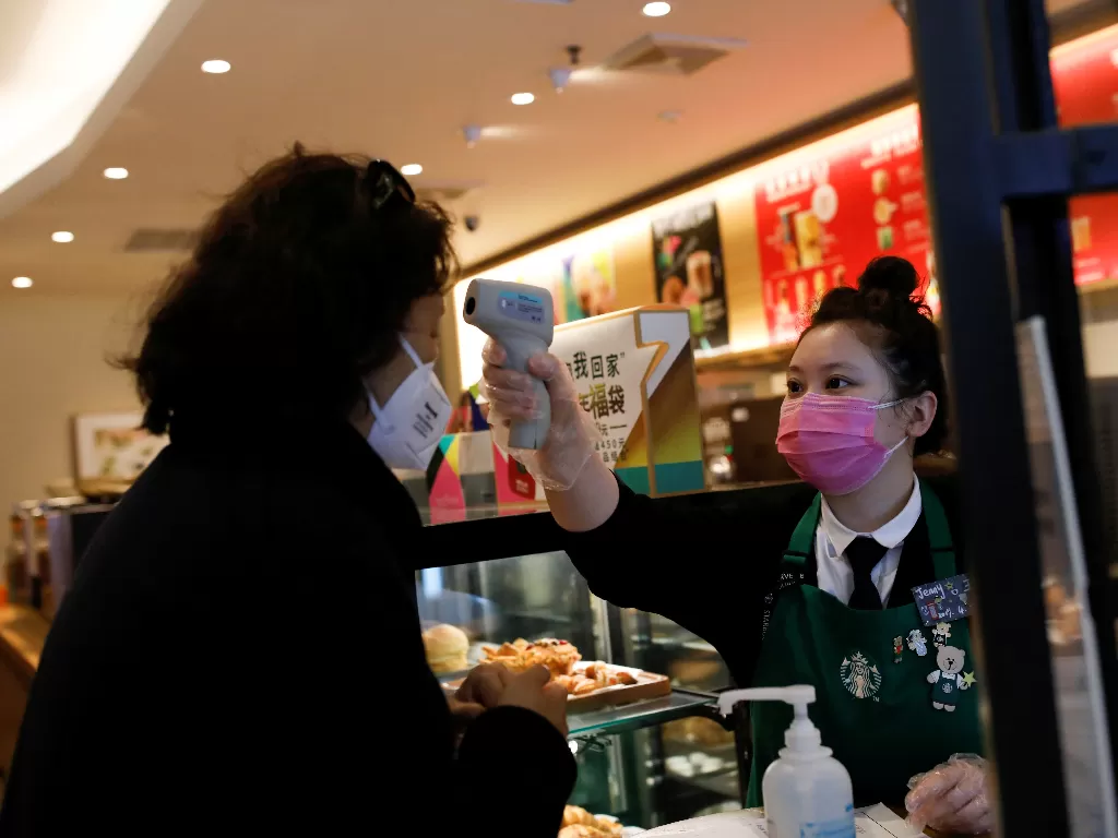 Seorang pekerja menggunakan termometer untuk mengecek suhu tubuh pelanggan yang masuk ke dalam gerai Starbucks di Beijing, Tiongkok (30/1). (REUTERS/Carlos Garcia Rawlins)