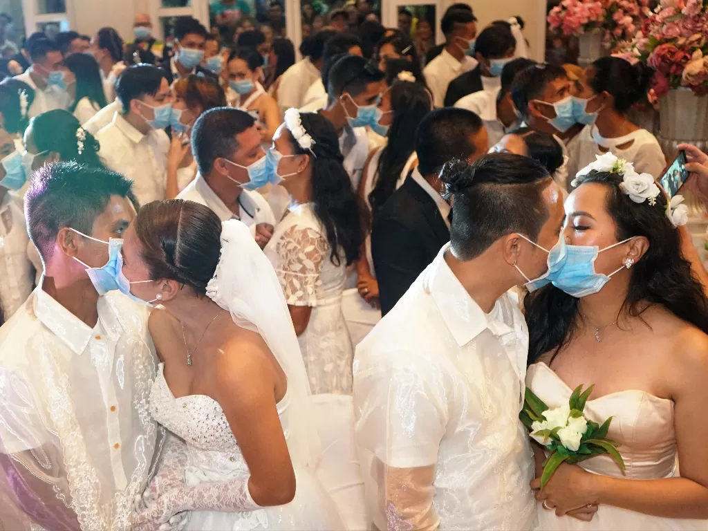 Pasangan Filipina mencium sambil mengenakan masker dalam pernikahan massal yang disponsori pemerintah di Kota Bacolod. (photo/Reuters/Bacolod City Public Information Office)