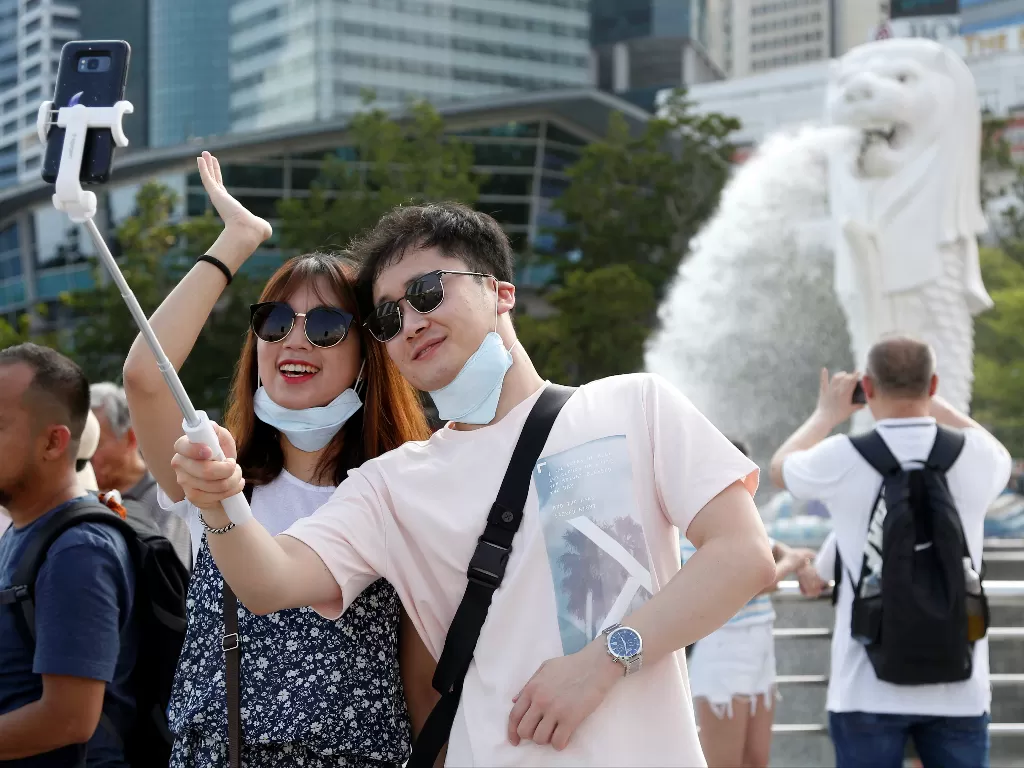 Ilustrasi - Turis yang memakai masker serta berpose untuk foto di Taman Merlion di Singapura. (photo/Reuters/Feline Lim)