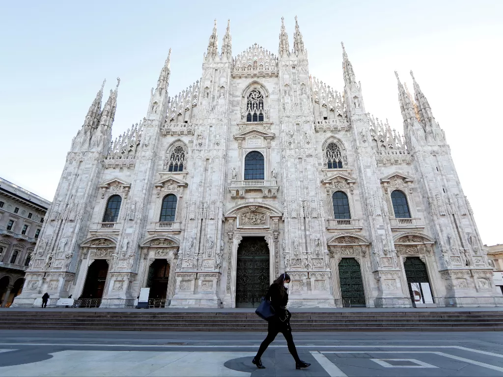 Seorang wanita mengenakan masker pelindung berjalan melalui alun-alun Duomo, saat wabah koronavirus terus tumbuh di Italia utara, di Milan. (photo/Reuters/Yara Nardi)