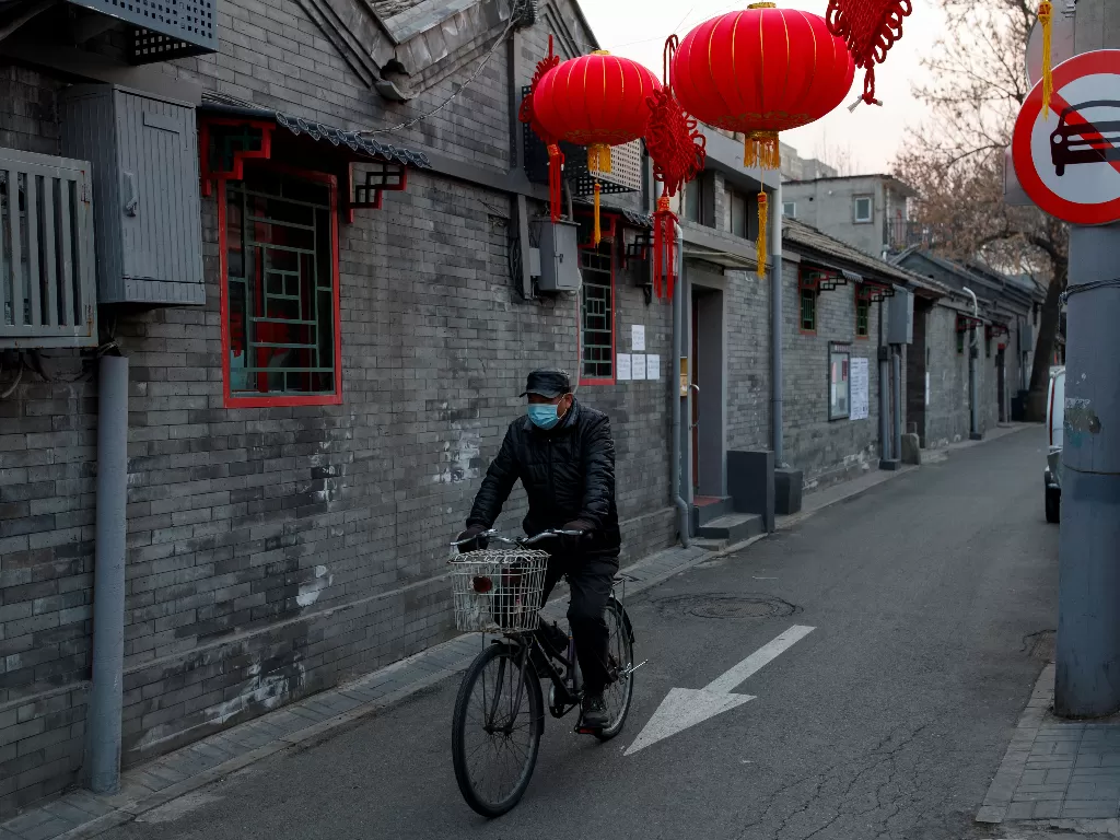 Seorang pesepeda mengenakan masker melintasi sebuah gang kecil yang sepi di Beijing (25/2). (REUTERS/Thomas Peter)