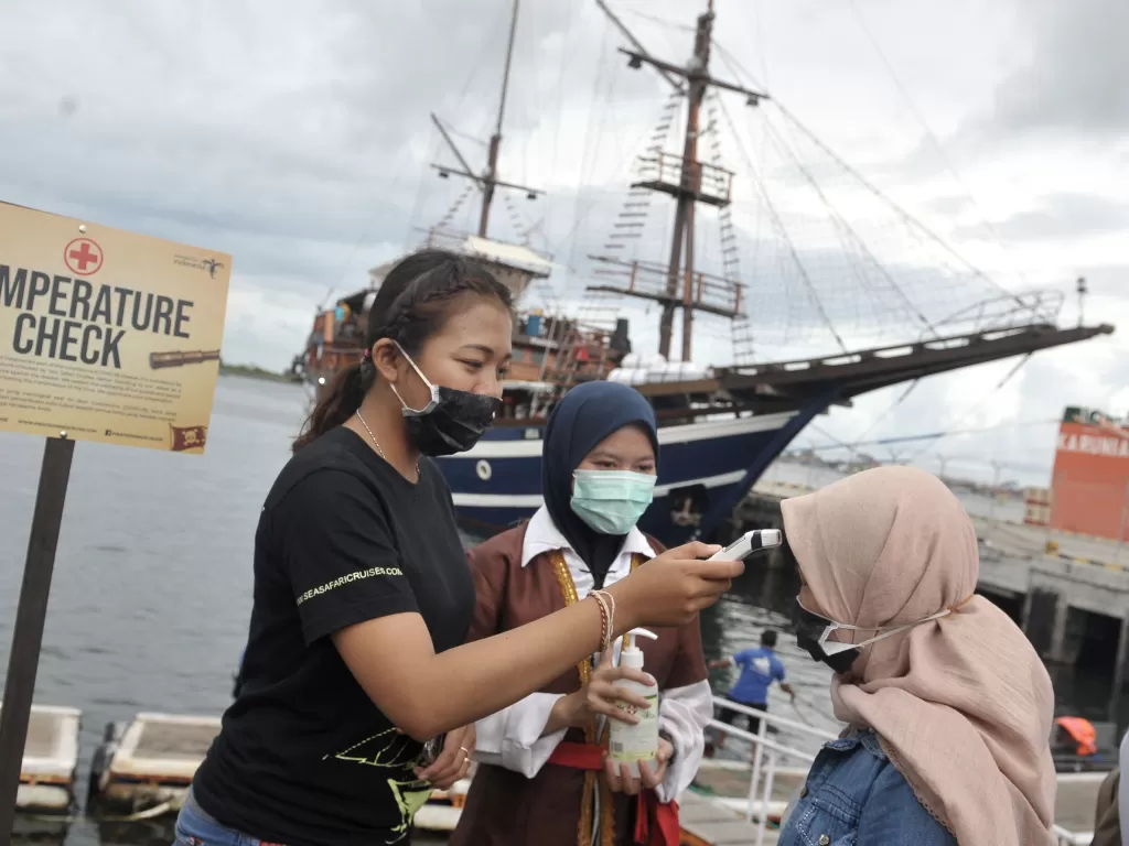 Petugas memeriksa suhu tubuh wisatawan yang akan menikmati atraksi wisata Pirate Dinner Cruise di atas kapal Sea Safari Cruise 9 di Pelabuhan Benoa, Denpasar, Bali, Jumat (6/3). (ANTARA FOTO/Fikri Yusuf)