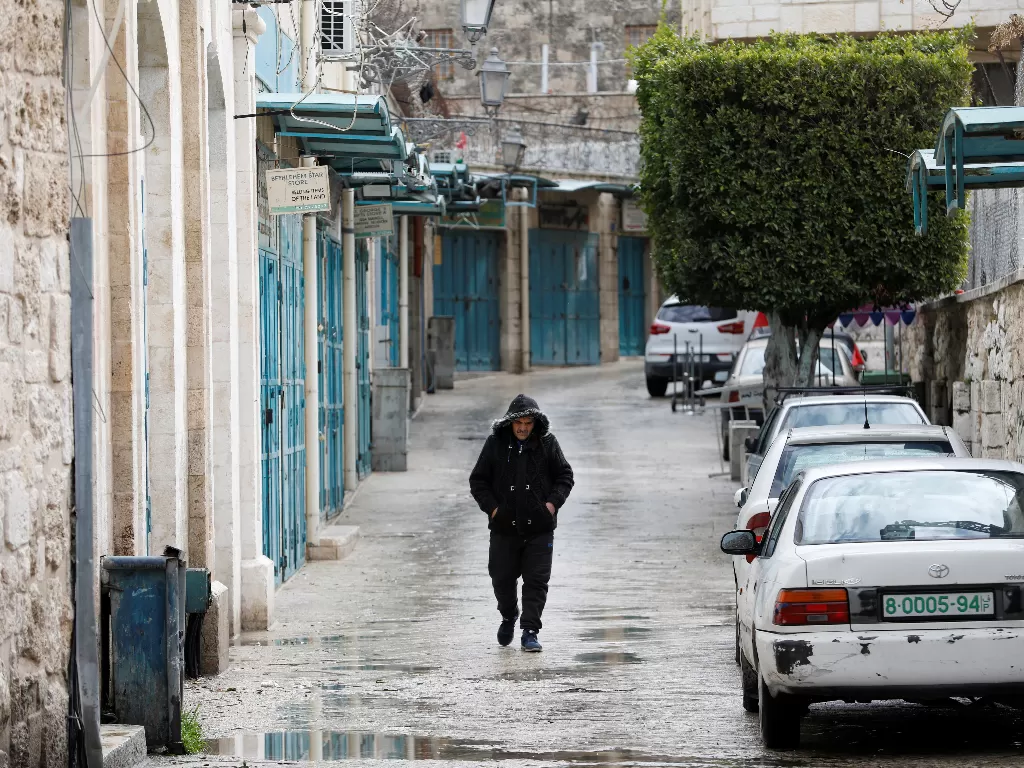 Seorang pria berjalan melewati toko-toko yang tutup setelah tindakan pencegahan diambil terhadap virus corona, di Betlehem di Tepi Barat yang diduduki Israel. (photo/Reuters/Mussa Qawasma)