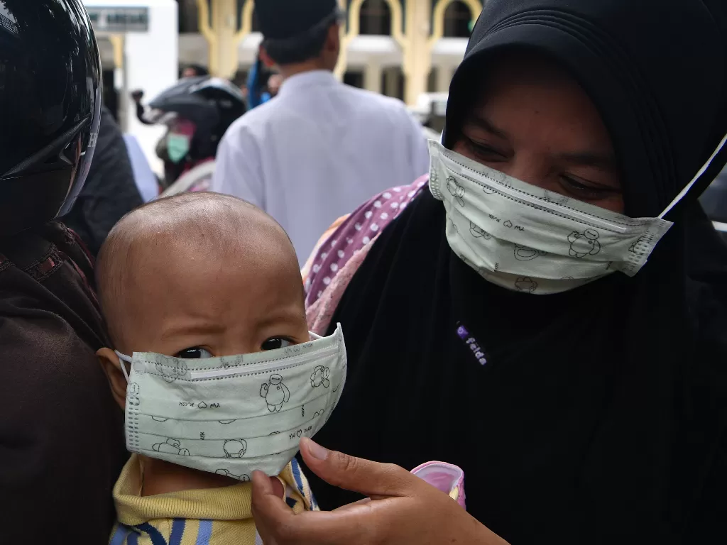 Seorang ibu memakaikan masker pada anaknya untuk mencegah penyebaran virus corona saat Lembaga Falakiyah PCNU Gresik membagikan masker gratis di Gresik, Kamis (5/3/2020). (ANTARA FOTO/Zabur Karuru)
