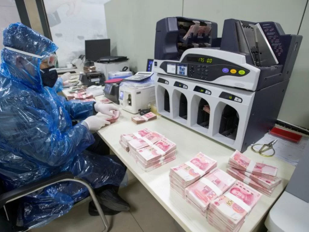 Seorang pekerja menggunakan jas hujan plastik dengan masker wajah dan kacamata pelindung saat menyortir uang kertas yuan China di sebuah bank di Taiyuan, provinsi Shanxi, Tiongkok, Senin (24/2/2020). (Cnsphoto via REUTERS)