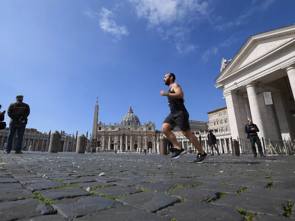 Seorang warga berolahraga lari-lari kecil di sekitar kawasan St. Peter's Square di saat lockdown masih diterapkan pemerintah Italia di Roma, Minggu (15/3). (REUTERS/Alberto Lingria)