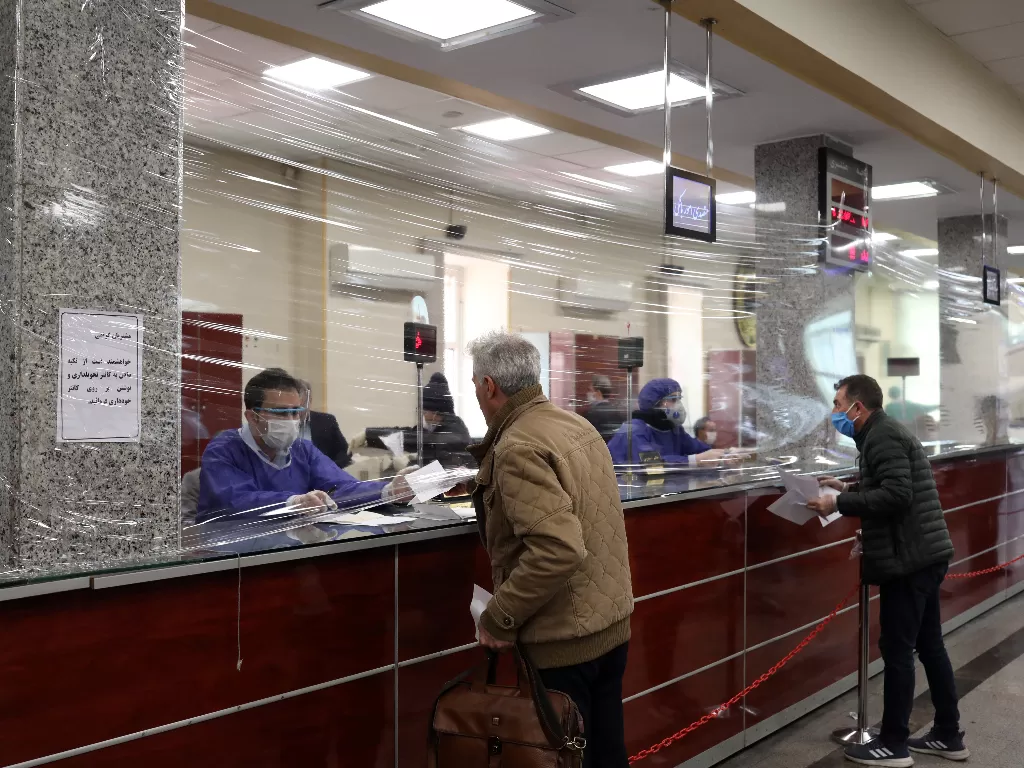Sebuah penutup plastik memisahkan antara pegawai bank dan pengunjung untuk mengantisipasi penyebaran wabah virus corona di Tehran, Iran, Selasa (17/3/2020). (WANA/Ali Khara via REUTERS)