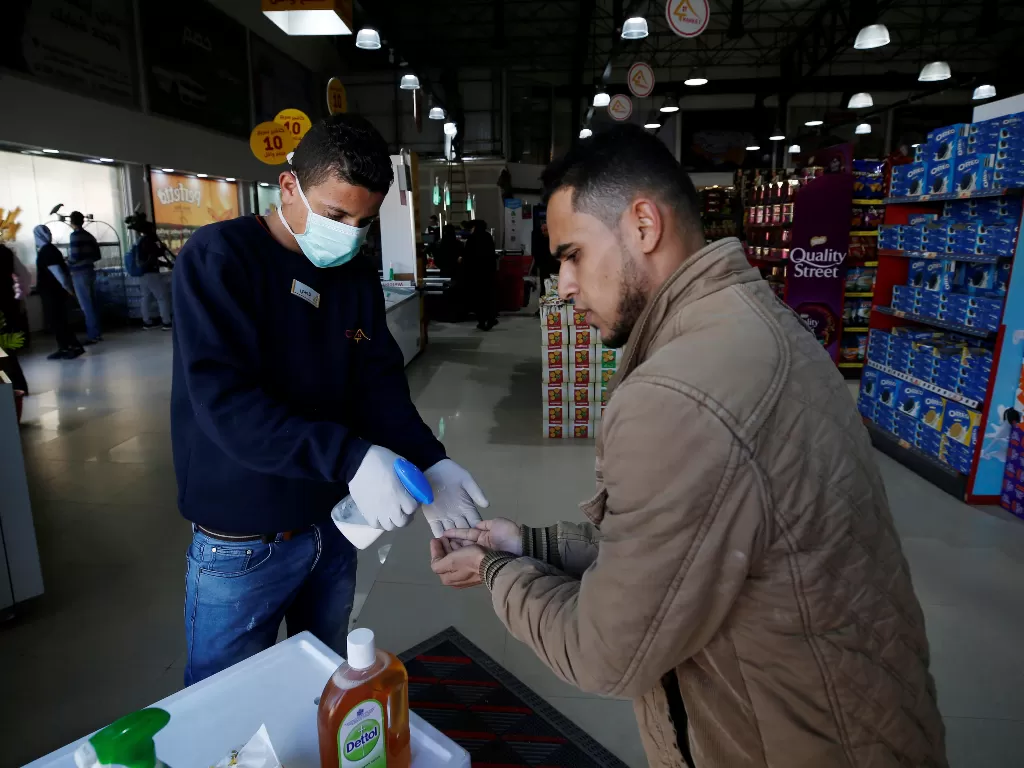 Seorang pekerja supermarket di Palestina memberi hand sanitizer kepada pengunjung (REUTERS/Mohammed Salem)