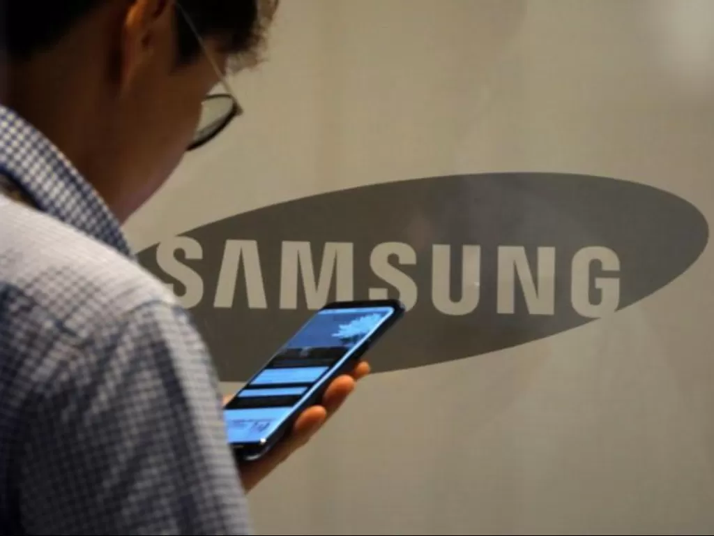 Seorang pria sedang menggunakan smartphone di depan logo Samsung (photo/REUTERS/Kim Hong-Ji)