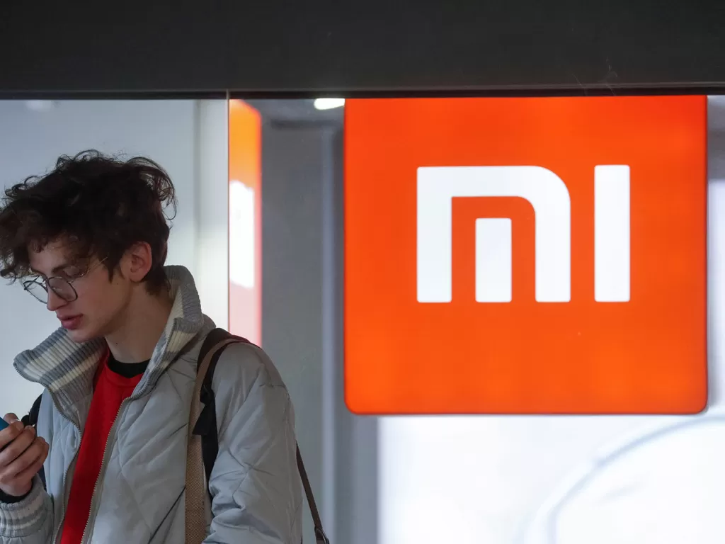 Seorang pria sedang berada di sebelah logo Xiaomi (photo/REUTERS/Valentyn Ogirenko)