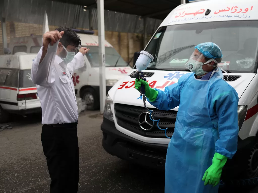 Ilustrasi: Seorang anggota staf medis darurat didesinfeksi setelah memindahkan seorang pasien dengan penyakit coronavirus (COVID-19) di Teheran. (WANA via REUTERS)