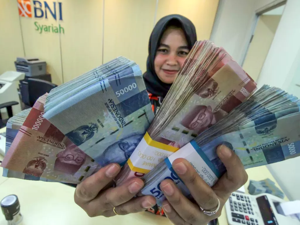 Ilustrasi: petugas bank menunjukkan uang saat melayani penarikan uang nasabah di bank BNI Syariah Lhokseumawe, Aceh, Jumat (13/3/2020). (ANTARA/Rahmad)