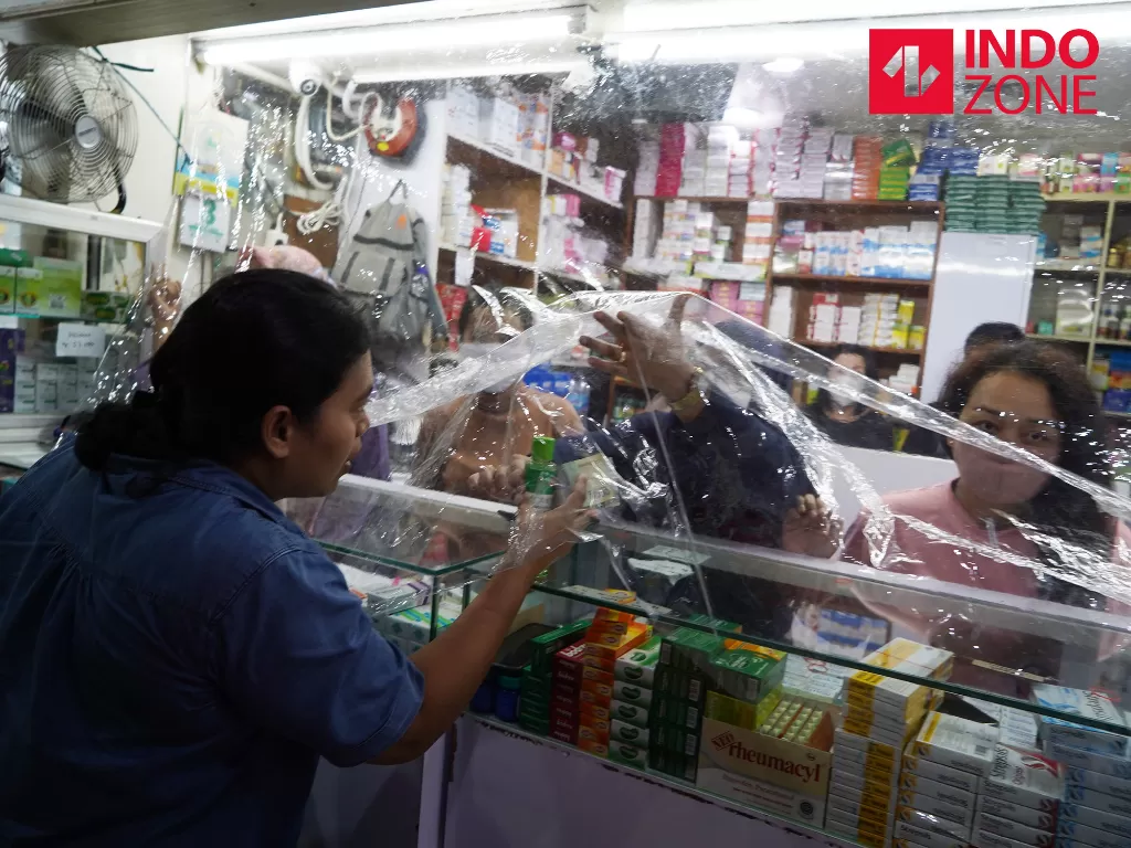 Pekerja melayani pembeli dari balik plastik pembatas di apotek di kawasan Pasar Baru, Jakarta, Jumat (3/4/2020). (INDOZONE/Arya Manggala)
