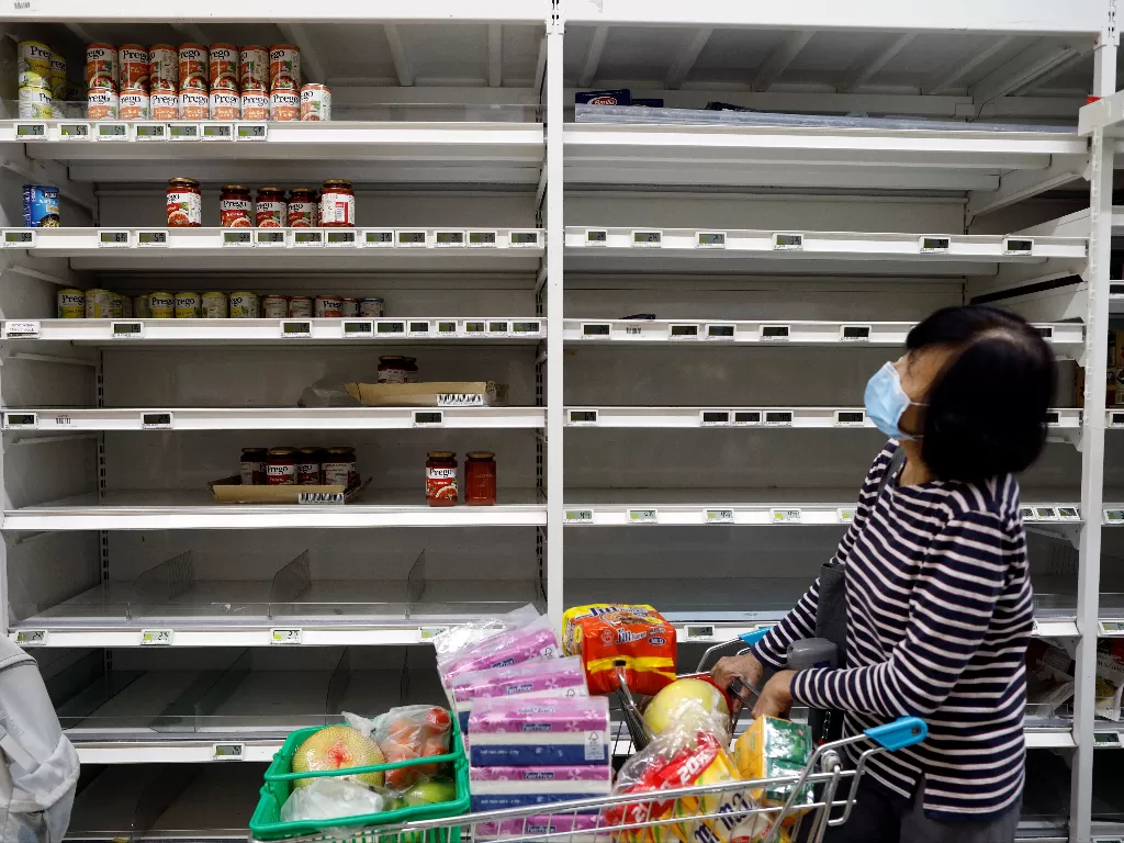 Seorang wanita mengenakan masker berjalan melewati rak-rak kosong di supermarket, Singapura. (Photo/REUTERS/Edgar Su)