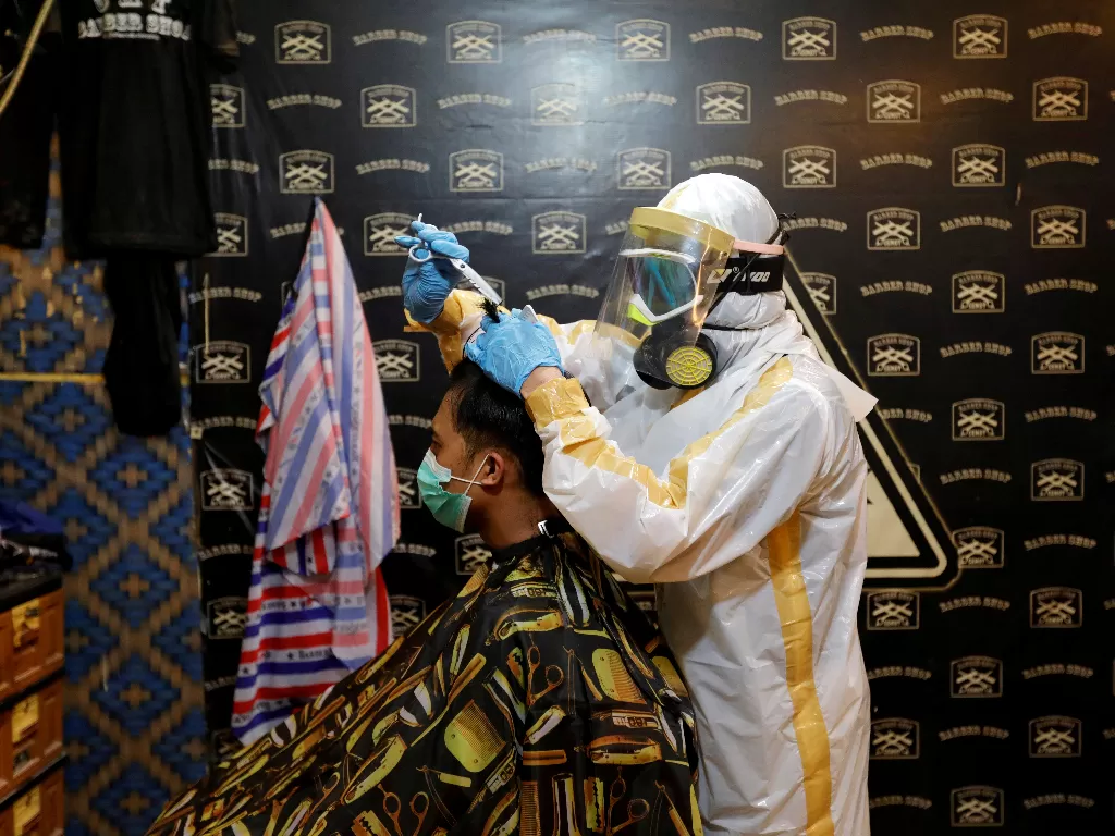 Seorang tukang cukur menggunakan alat pelindung diri (APD) saat mencukur rambut pelanggannya di tempat pangkas rambut Chemot Barbershop, Ciawi, Bogor, Jawa Barat, Senin (6/4/2020). (REUTERS/Willy Kurniawan)
