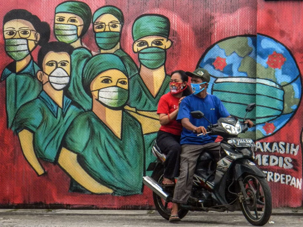 Pengendara motor melintas di depan mural tentang pandemi virus corona di Jalan Raya Jakarta-Bogor, Depok, Jawa Barat. (ANTARA/Yulius Satria Wijaya)