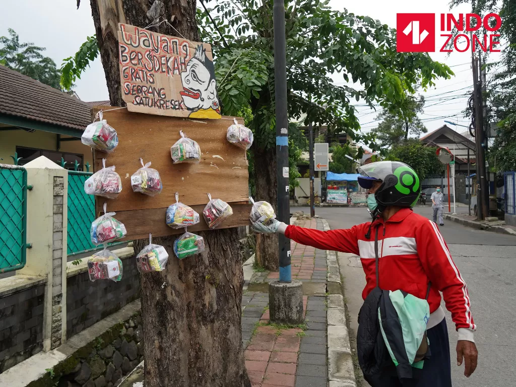 Warga mengambil paket sembako yang digantung di pohon di Jalan Cawang Baru Utara, Jakarta, Rabu (15/4/2020). (INDOZONE/Arya Manggala)