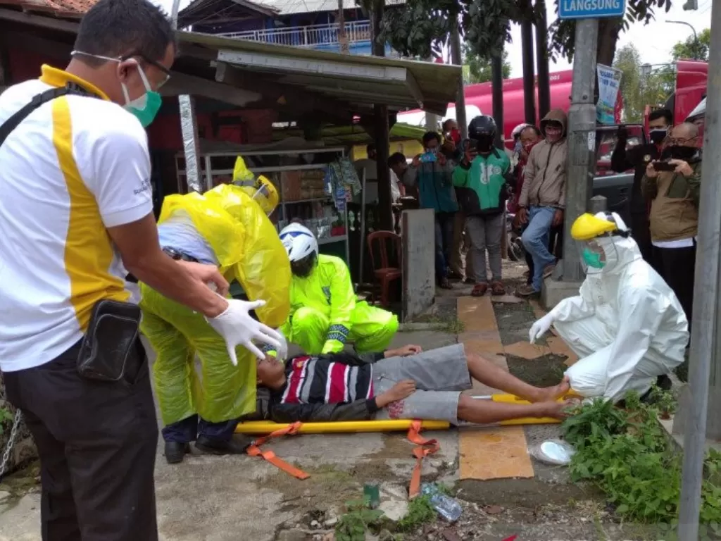 Anggota Polantas Polres Sukabumi Kota yang hanya dengan menggunakan jas hujan sebagai APD saat membantu tim medis mengevakuasi seorang warga yang terkapar. (ANTARA/Aditya Rohman)