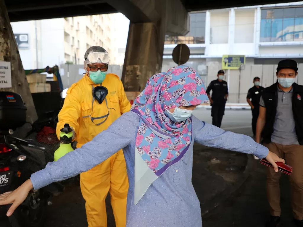 Ilustrasi: seorang pekerja menyemprotkan desinfektan pada seorang wanita selama perintah kontrol gerakan karena wabah penyakit coronavirus (COVID-19), di Kuala Lumpur (REUTERS/Lim Huey Teng)