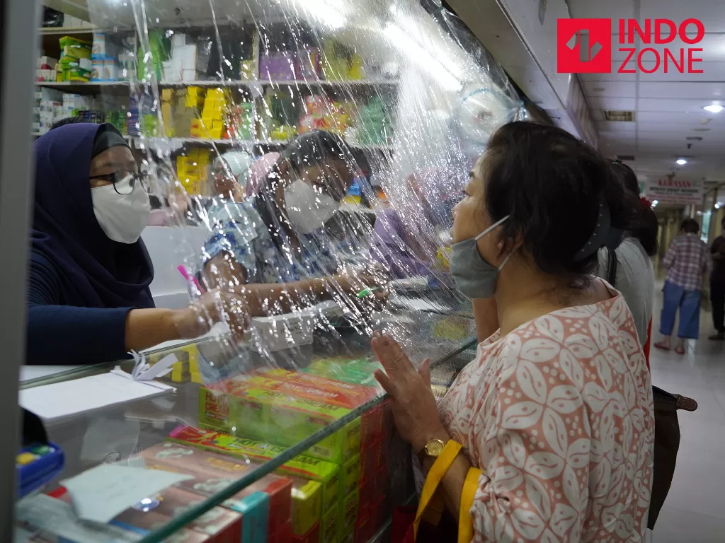 Pekerja melayani pembeli dari balik plastik pembatas di apotek di kawasan Pasar Baru, Jakarta, Jumat (3/4/2020). (INDOZONE/Arya Manggala)
