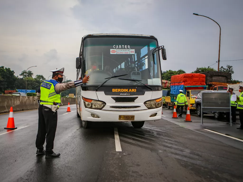 Petugas kepolisian mengarahkan bus ke pintu keluar Tol Bitung, Kabupaten Tangerang, Banten, Jumat (24/4/2020). (ANTARA FOTO/Fauzan)