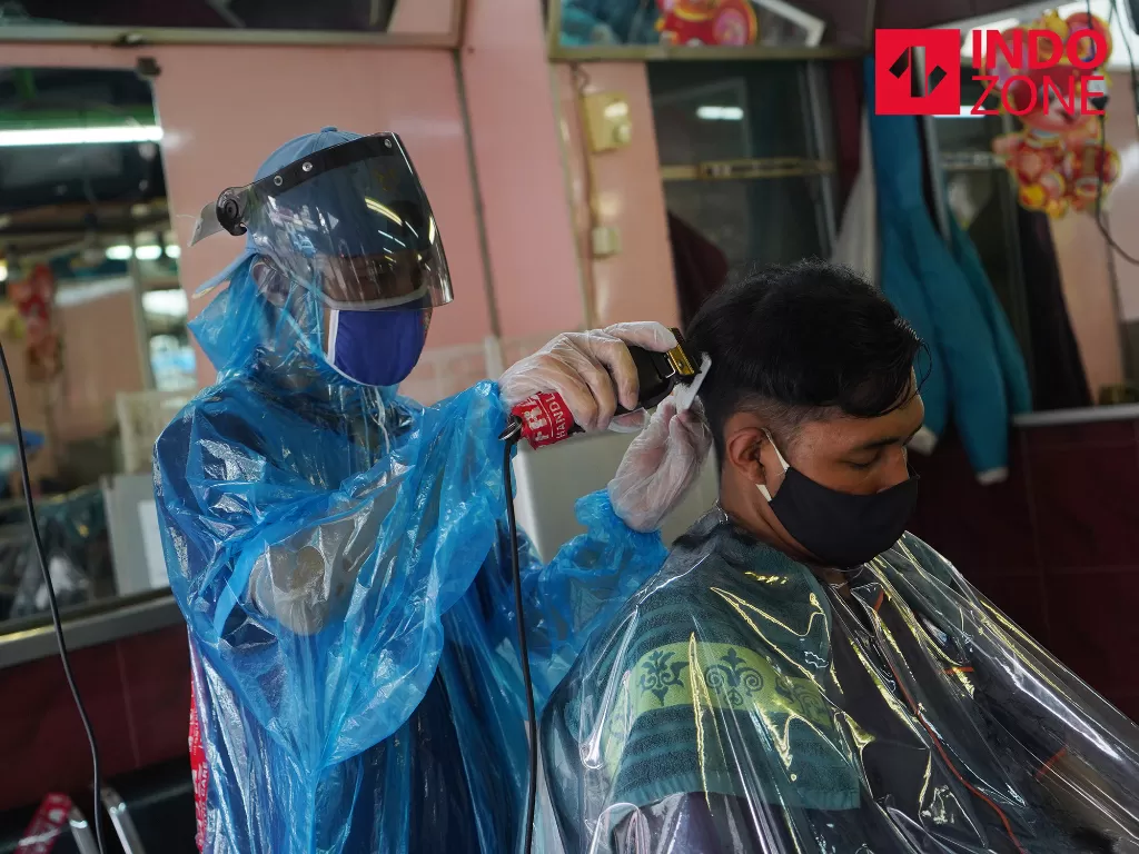  Tukang cukur memakai Alat Pelindung Diri (APD) buatan sendiri saat mencukur rambut pelanggannya di Pondok Kelapa, Jakarta Timur, Selasa (28/4/2020). (INDOZONE/Arya Manggala)