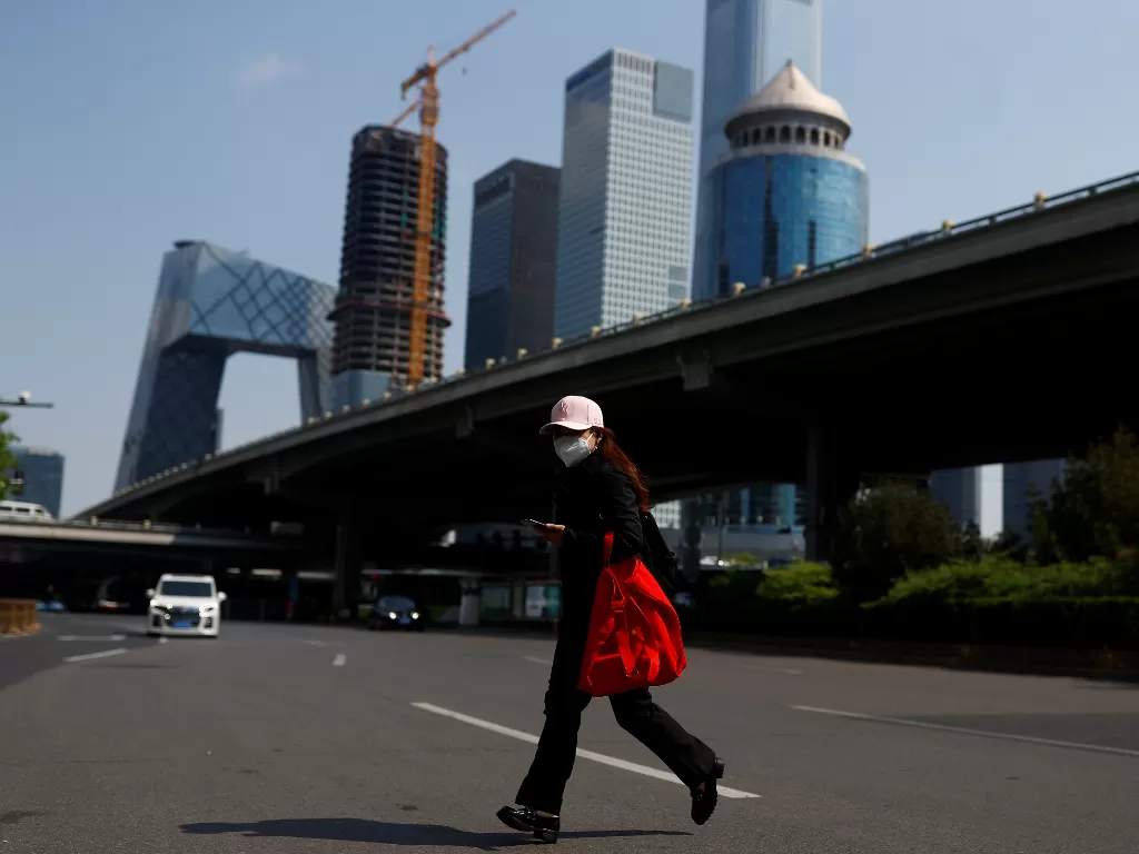 Seorang wanita melintasi sebuah jalan di Kawasan Pusat Bisnis Beijing pada jam sibuk pagi hari saat penyebaran penyakit Covid-19 di Tiongkok. (Photo/REUTERS/Thomas Peter)