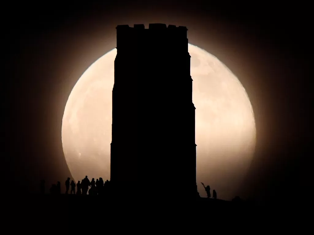 Orang-orang terlihat di Glastonbury Tor di sebelah Menara St Michael saat bulan purnama Supermoon atau Flower Moon, Glastonbury, Inggris, 7 Mei 2020. (REUTERS/Toby Melville)