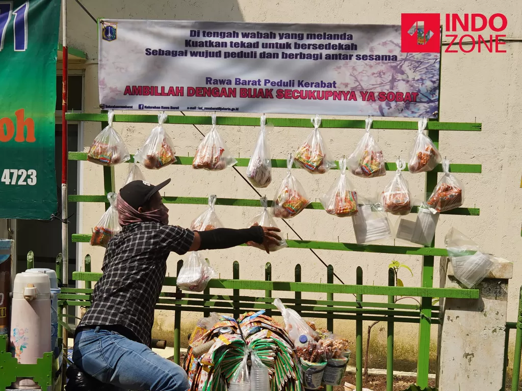 Warga mengambil paket sembako yang digantung di tiang berbagi sedekah di kawasan Kelurahan Rawa Barat, Jakarta, Kamis (14/5/2020). (INDOZONE/Arya Manggala)