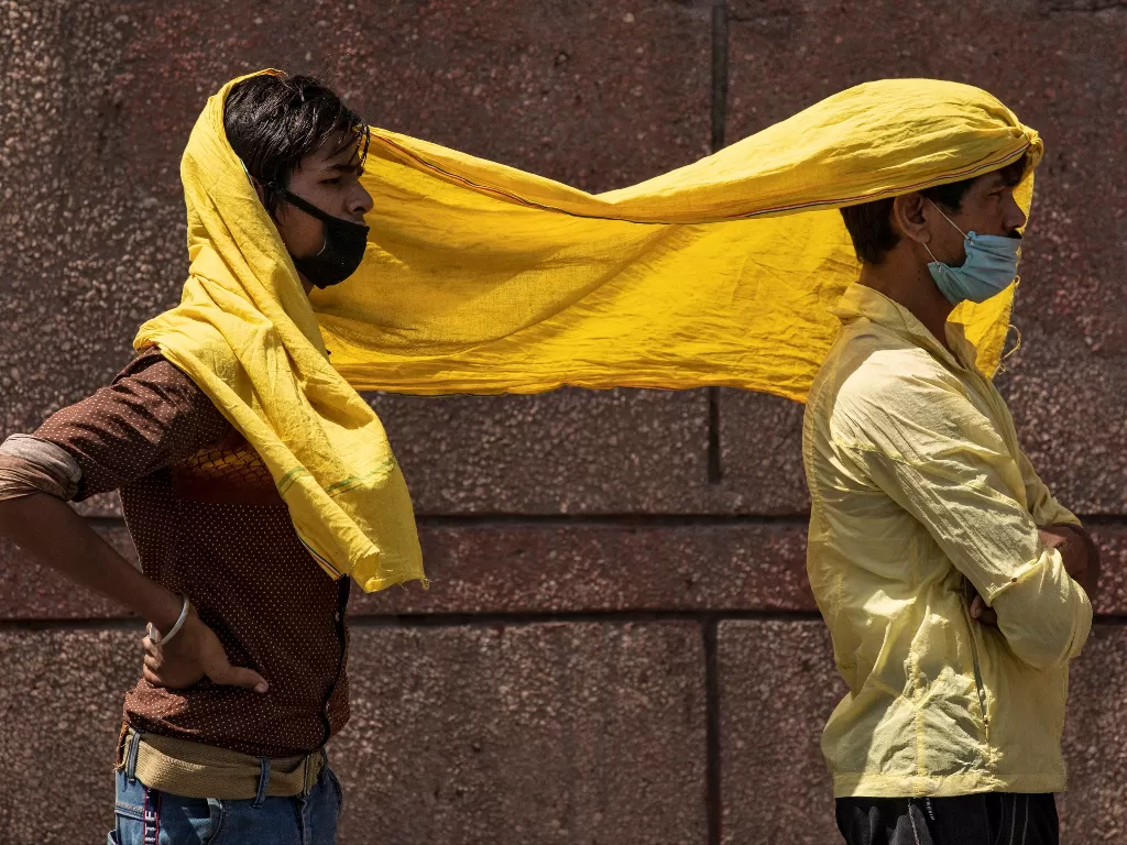 Pekerja migran menutupi diri mereka dengan syal, untuk melindungi dari panas ketika mereka menunggu untuk didaftarkan sebelum naik kereta ke negara asal mereka di Bihar timur. (Photo/REUTERS/Danish Siddiqui)