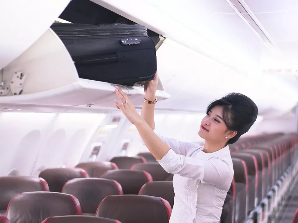Seorang pramugari dari salah satu maskapai milik Lion Air Group sedang mengatur tas penumpang di bagasi kabin pesawat. (Instagram/@lionairgroup)