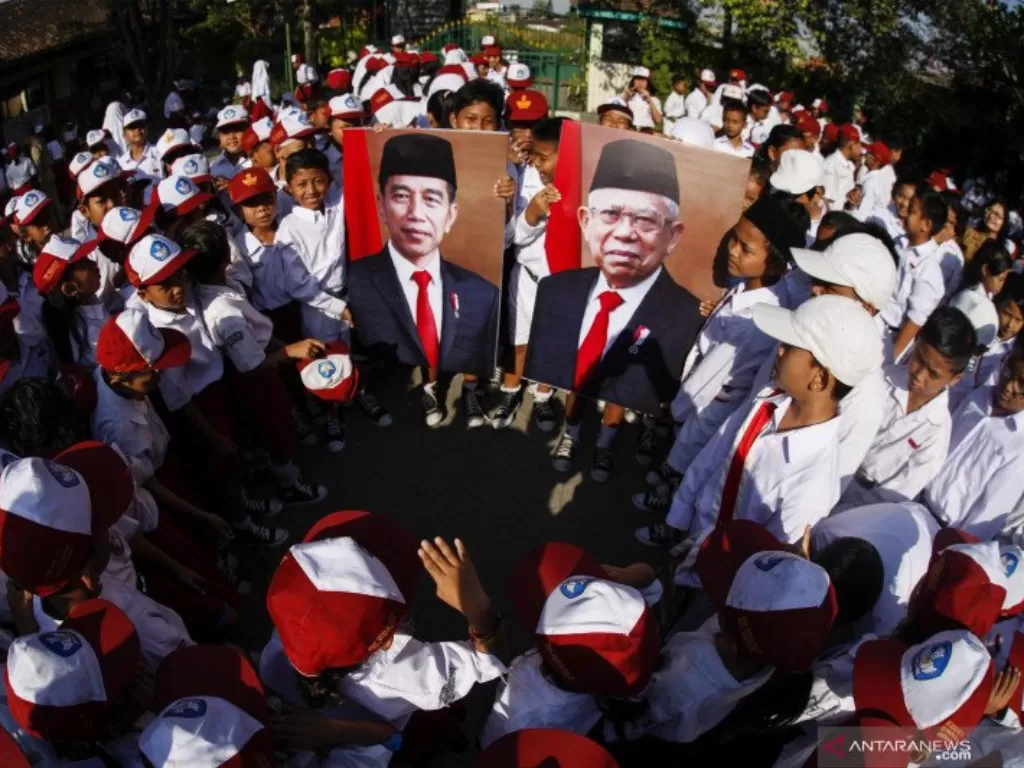 Siswa SD Negeri Joglo Solo membawa foto Presiden Joko Widodo dan dan Wakil Presiden Ma'ruf Amin usai upacara bendera di sekolahnya di Solo, Jawa Tengah, sebelum pandemi terjadi. (ANTARA FOTO/Maulana Surya)