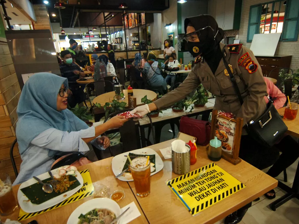 Petugas kepolisian membagikan masker kepada pengunjung restoran saat persiapan penerapan normal baru di salah satu mal di Tegal (ANTARA FOTO/Oky Lukmansyah)